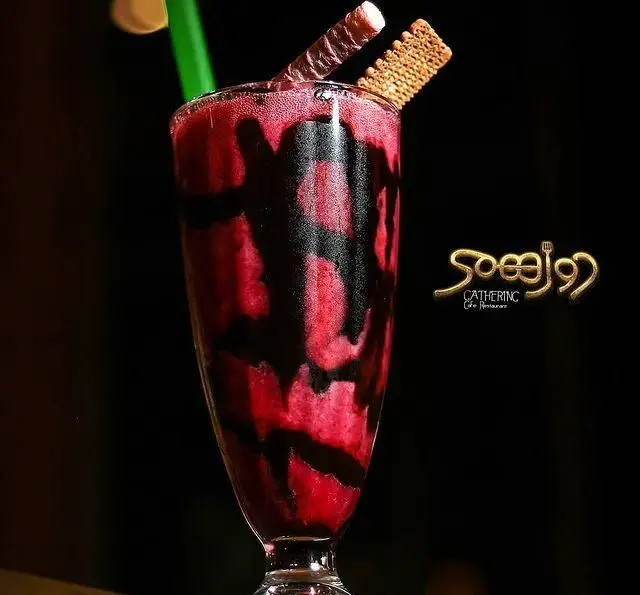 نوشیدنی خنک و جذاب دورهمی: شیک میوه‌ای قرمز با سس شکلات، تزیین شده با ویفر و بیسکویت. بهترین انتخاب در کافه رستوران دورهمی.