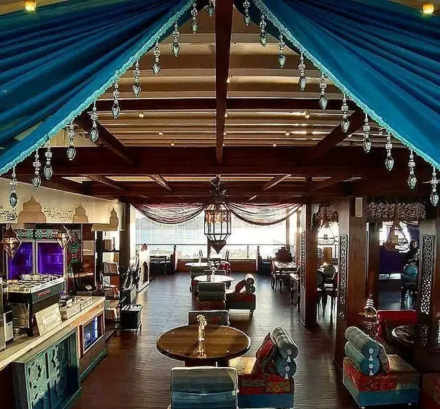فضای داخلی گرم و دلنشین رستوران و کافی شاپ دورهمی با دکوراسیون سنتی، پرده‌های آبی سقفی، لوستر زیبا و مبلمان راحت.