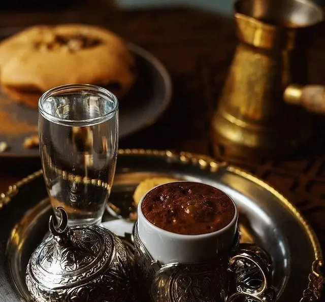 سرو قهوه سنتی و دلپذیر در رستوران و کافی شاپ دورهمی: فنجان قهوه، لیوان آب، قندان نقره‌ای و دسر، تجربه‌ای اصیل.