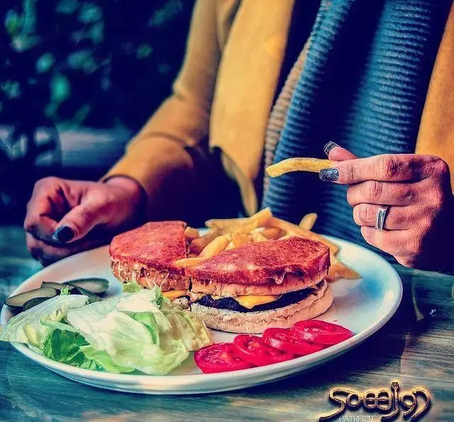 زن در حال میل کردن برگر و سیب زمینی سرخ کرده در رستوران و کافی شاپ دورهمی. غذای با کیفیت و محیطی دلنشین برای مشتریان.