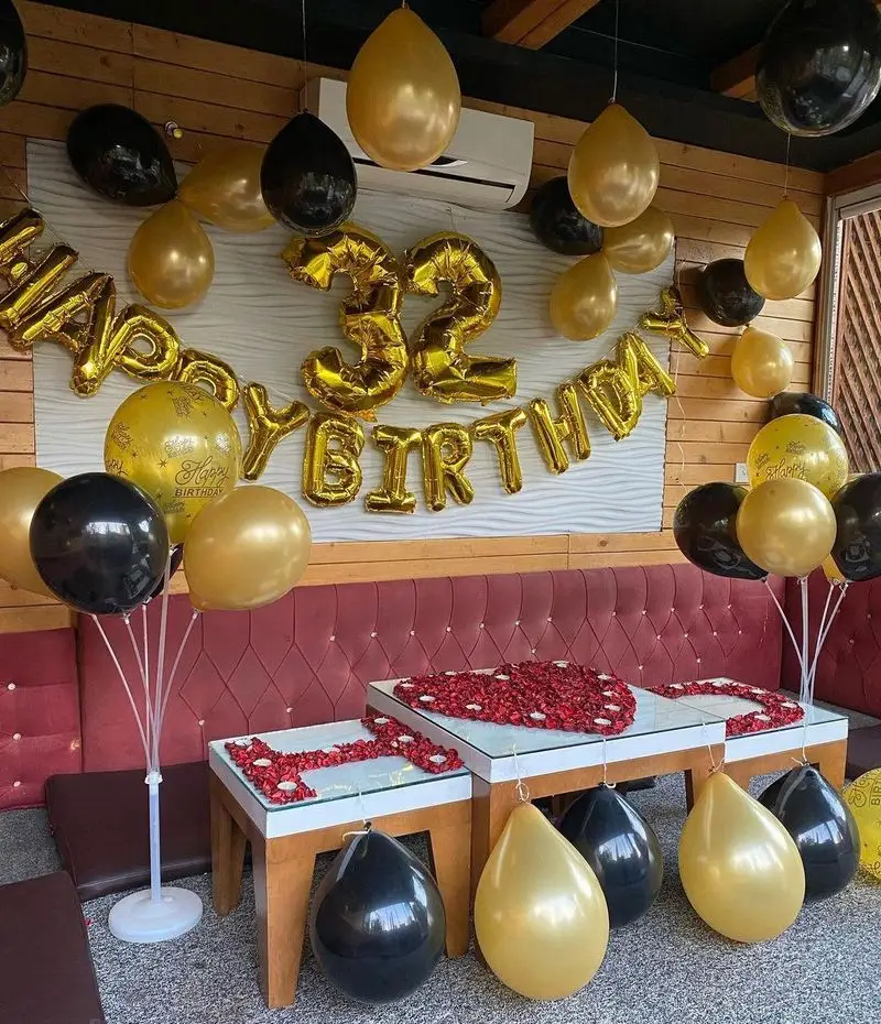 جشن تولد ۳۲ سالگی باشکوه در رستوران و کافی شاپ دورهمی با بادکنک‌آرایی طلایی، مشکی، میزآرایی رمانتیک و فضای گرم و دلنشین.