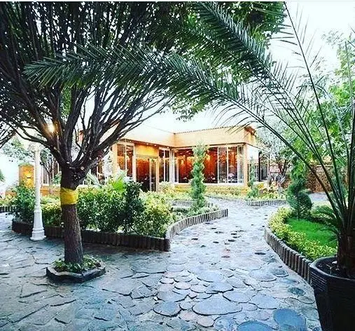 نمایی زیبا از فضای سبز و باغ رستوران و کافی شاپ دورهمی، با مسیر سنگی و درختان سرسبز، محیطی دلنشین برای پذیرایی از شما.