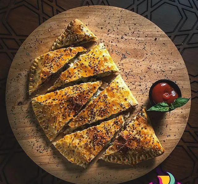 کالزونه لذیذ و طلایی برش‌خورده، با دانه‌های خوش‌عطر و سس کچاپ، در فضای دلنشین رستوران و کافی شاپ دورهمی برای تجربه‌ای بی‌نظیر.