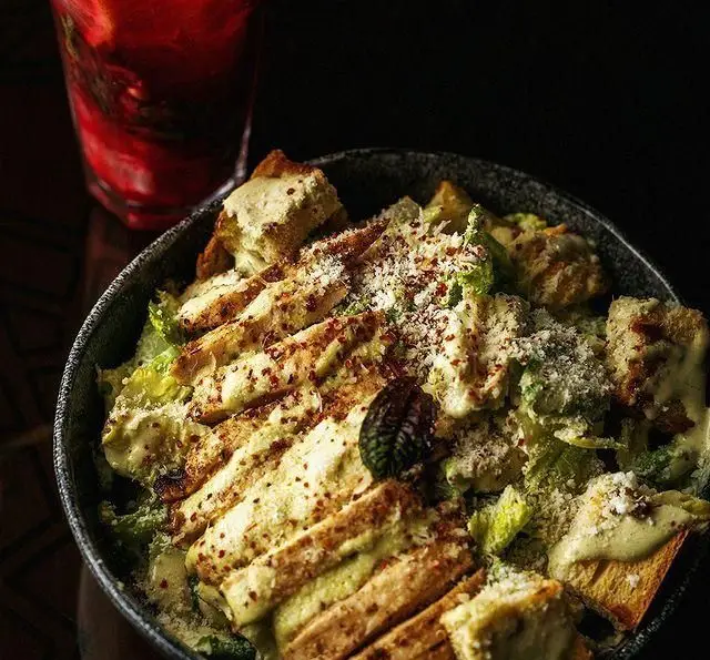 سالاد سزار مرغ لذیذ و تازه با پنیر فراوان و کروتون‌های ترد، در کنار نوشیدنی در فضای دلنشین رستوران دورهمی.