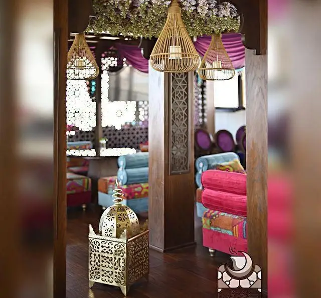 دکوراسیون داخلی رستوران و کافی شاپ دورهمی با مبلمان سنتی رنگارنگ، لوسترهای حصیری و فانوس‌های فلزی قلم‌زنی‌شده.