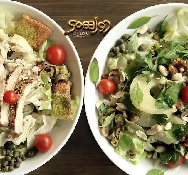 دو بشقاب سالاد تازه و خوشمزه از منوی رستوران و کافی شاپ دورهمی، شامل سالاد سزار مرغ و سالاد سبز با مغزیجات سالم.