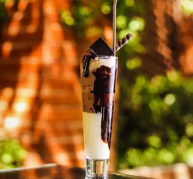 میلک شیک شکلاتی یا دسر لایه ای دلچسب با سس شکلات و تزئینات زیبا در فضای دلنشین رستوران و کافی شاپ دورهمی.