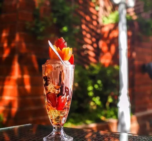 دسری خنک و لذیذ؛ بستنی میوه‌ای با سس شکلات و تزئینات زیبا در فضای دلنشین رستوران و کافی شاپ دورهمی.