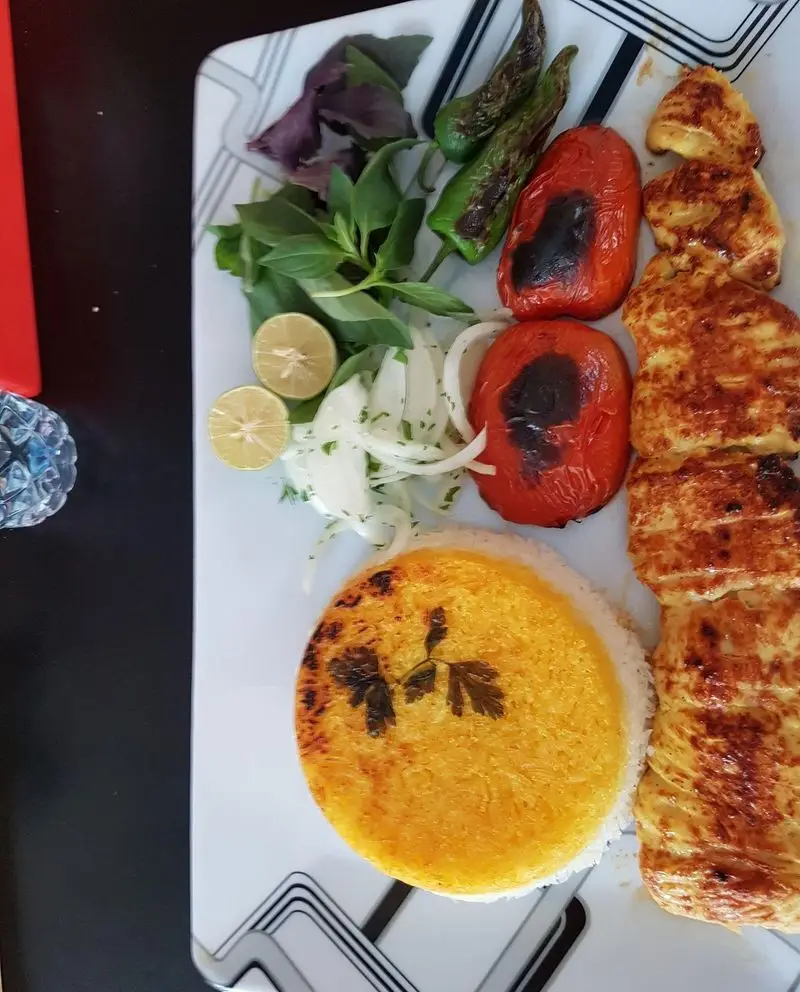 کباب جوجه زعفرانی با برنج ته دیگی طلایی، گوجه و فلفل کبابی. غذای سنتی و لذیذ ایرانی از رستوران و فست فود بریکا. سرو با مخلفات.