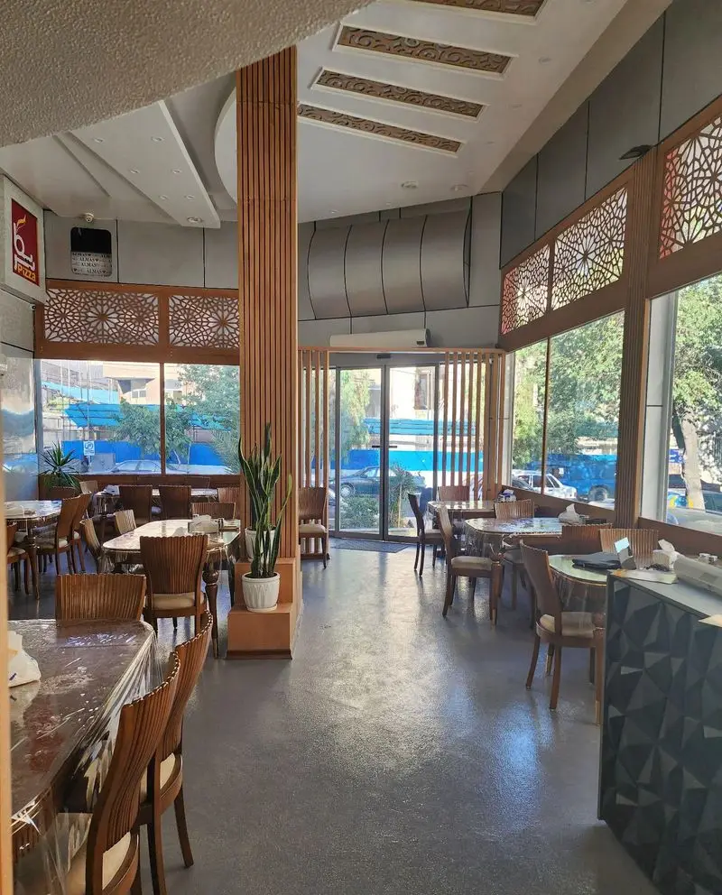 رستوران ایرانی و فست فود بریکا: فضای داخلی دلباز و مدرن با میز و صندلی‌های چوبی، پنجره‌های بزرگ و سقف دکوراتیو.