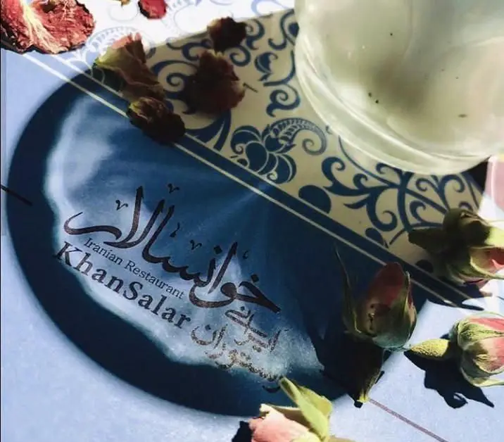 تصویری از لوگو و نام "رستوران ایرانی خوانسالار" با خط نستعلیق زیبا، در محیطی دلنشین با تزئین گل رز و عناصر سنتی.