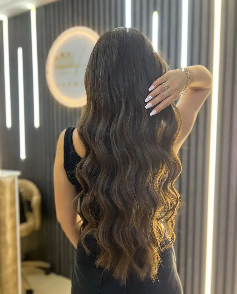 نمونه کار جذاب کرلی موی بلند و حالت‌دار دخترانه با رنگ قهوه‌ای تیره و براق در سالن زیبایی و آرایشی تخصصی مدرن
