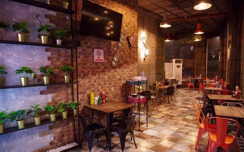 فضای داخلی شیک و مدرن فست فود سه فر با میز و صندلی‌های چوبی و فلزی، دیوار آجری و دکوراسیون خاص برای تجربه غذایی دلپذیر.