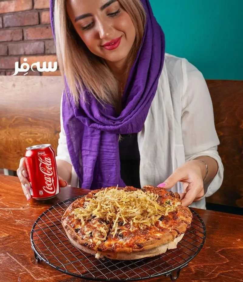 تجربه لذت‌بخش در فست فود سه فر: زن جوان در حال لذت بردن از پیتزای خوشمزه با سیب‌زمینی سرخ‌کرده فراوان و نوشابه کوکاکولا است.