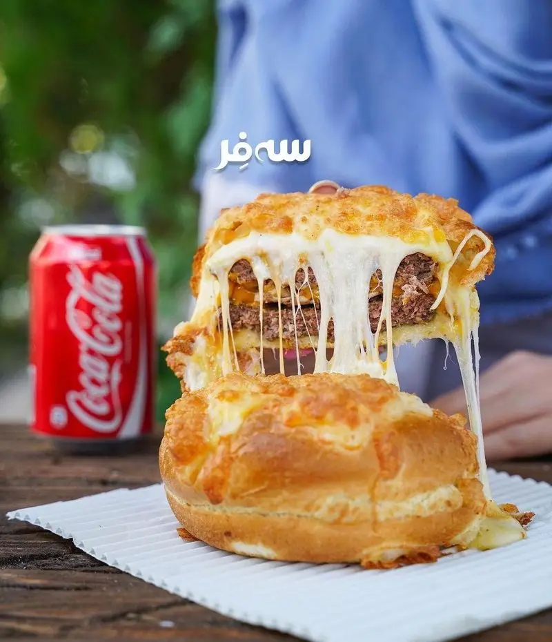 دوبل چیزبرگر پر پنیر فست فود سه فر با لایه های گوشت و پنیر آب شده کشدار و جذاب، در کنار نوشیدنی کوکاکولای خنک و دلپذیر. لذت غذایی عالی.