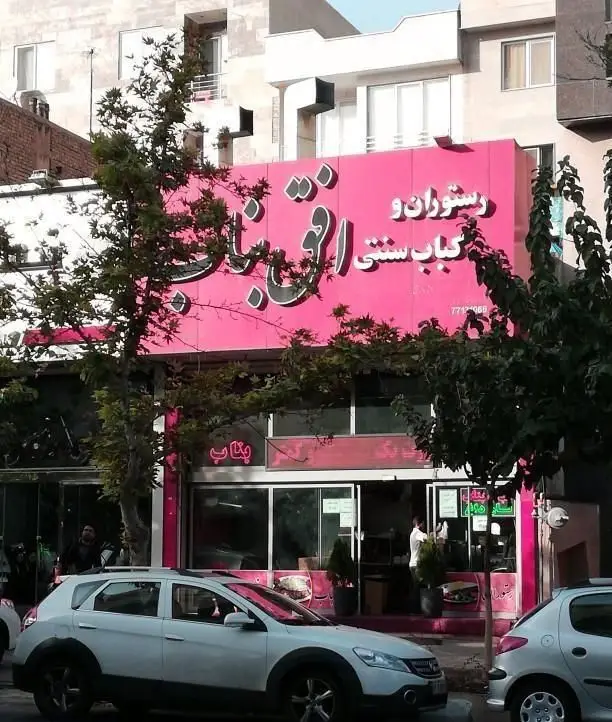 نمای بیرونی رستوران و کبابی سنتی افق بناب با تابلوی صورتی بزرگ، واقع در خیابان با ماشین‌ها و درختان در اطراف، عرضه کباب اصیل بناب.