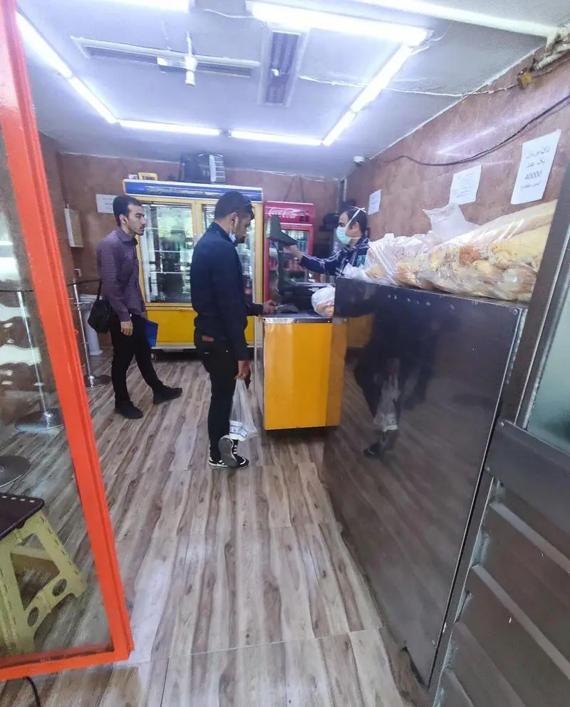 نمای داخل فروشگاه مرغ بریان ملاصدرا، شامل مشتریان و کارکنان با ماسک، نشان‌دهنده فعالیت و آماده‌سازی محصولات غذایی با رعایت بهداشت.