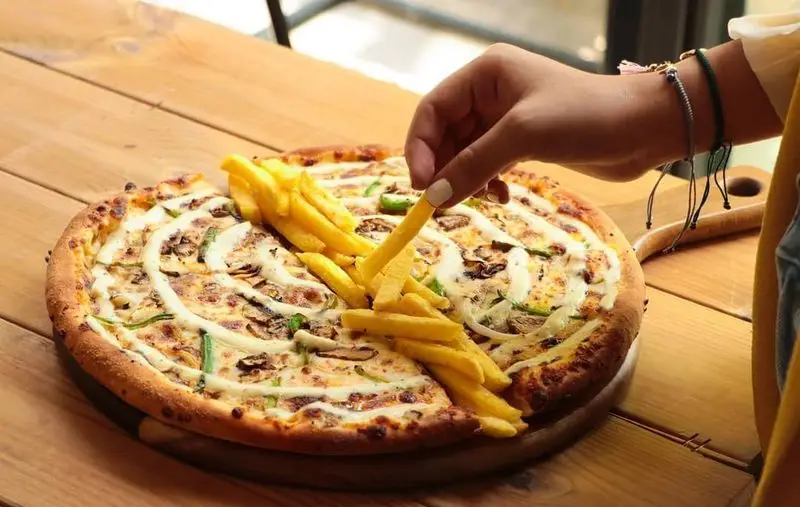 پیتزای داغ و تازه با تاپینگ سیب زمینی سرخ کرده در فست فود شیلا. دستی در حال برداشتن سیب زمینی از روی پیتزا برای مشتریان.