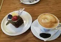 برش کیک شکلاتی با توت‌فرنگی و قهوه لاته روی میز چوبی در کافه قنادی اوریانت. بهترین شیرینی و نوشیدنی‌های گرم در اوریانت.