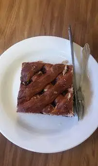 برش دسر شیرینی خوشمزه با رویه مشبک و قهوه‌ای از کافه قنادی اوریانت، روی بشقاب سفید با چنگال سرو شده است.