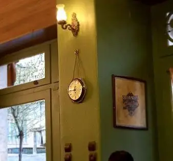 دکوراسیون داخلی کافه قنادی اوریانت با دیوار سبز، ساعت آویز و قاب عکس قدیمی؛ فضایی دلنشین برای تجربه شیرینی و قهوه.