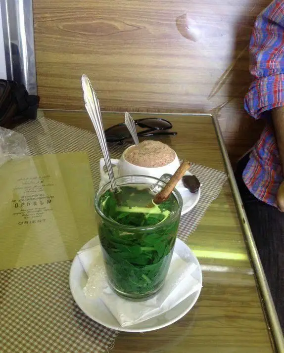 میزی در کافه قنادی اوریانت با یک فنجان چای نعناع تازه، قهوه داغ و منوی کافه. لذت نوشیدنی‌های گرم در محیطی دلنشین.