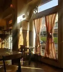 فضای دلنشین و روشن کافه قنادی اوریانت با نور طبیعی خورشید از پنجره‌ها، دکوراسیون داخلی شیک و میز و صندلی‌های راحت.