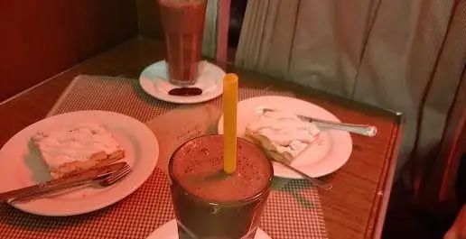 تصویری جذاب از نوشیدنی‌های شکلاتی و دو برش کیک یا دسر لذیذ در محیط دلپذیر کافه قنادی اوریانت، ایده‌آل برای یک عصرانه شیرین.