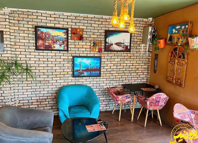 فضای داخلی جذاب و دنج کافه یونیس با دیوار آجری، تابلوهای هنری زیبا، مبلمان راحتی و صندلی‌های رنگارنگ پچ‌ورک، محیطی گرم و صمیمی.