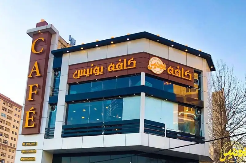 تصویر ساختمان مدرن و زیبای کافه یونیس، با نمای بیرونی شیک و تابلوهای "Cafe" و "کافه یونیس"، فضایی دلنشین برای کافه و رستوران.