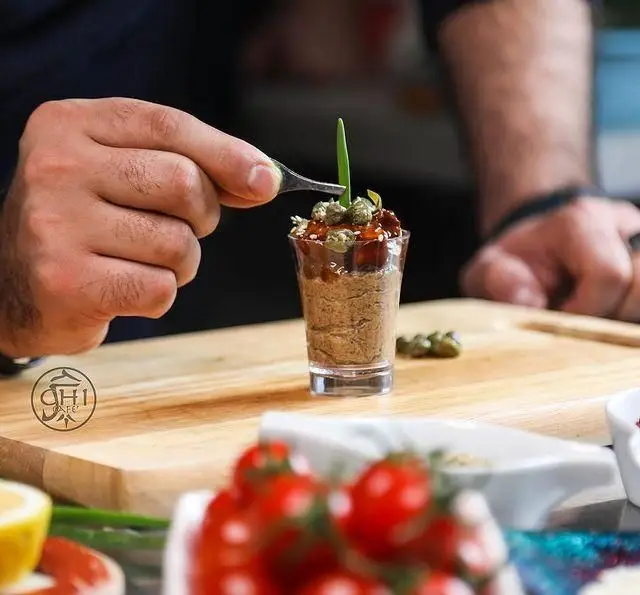 دستان آشپز چی کافه در حال دیزاین خلاقانه یک پیش‌غذای شیک و خوش‌طعم در لیوان شات، با تزئین هنرمندانه سبزیجات تازه.