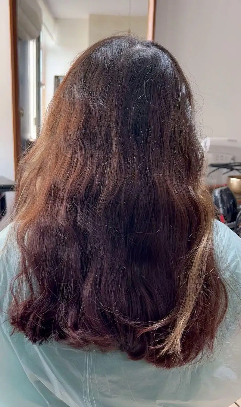 نمای پشت موهای بلند و موج دار مشتری با ریشه های تیره و ساقه های رنگ شده، آماده برای تغییر رنگ در سالن زیبایی کیانا