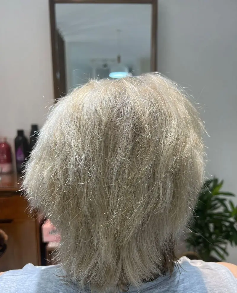تصویری از پشت سر مشتری با موهای بلوند روشن و کوتاهی شیک مدل شگی، پس از دریافت خدمات حرفه‌ای رنگ و کوتاهی در سالن زیبایی کیانا.