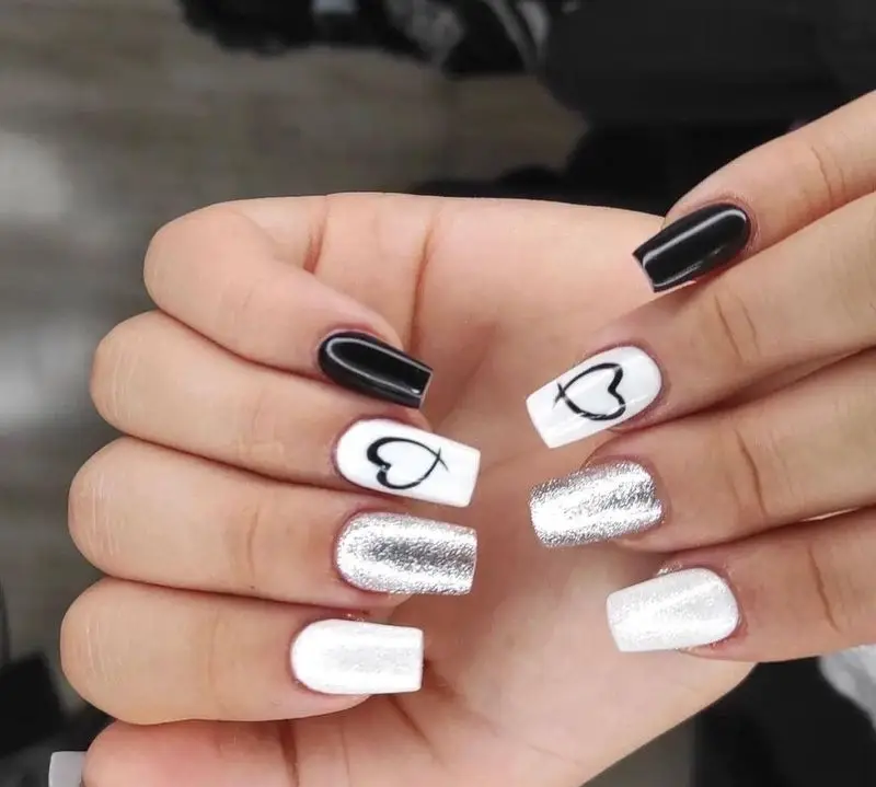 کاشت و طراحی ناخن شیک در سالن زیبایی کیانا: مانیکور با طرح‌های خاص مشکی، سفید، گلیتر نقره‌ای و قلب مینیمال، انتخابی زیبا برای شما.