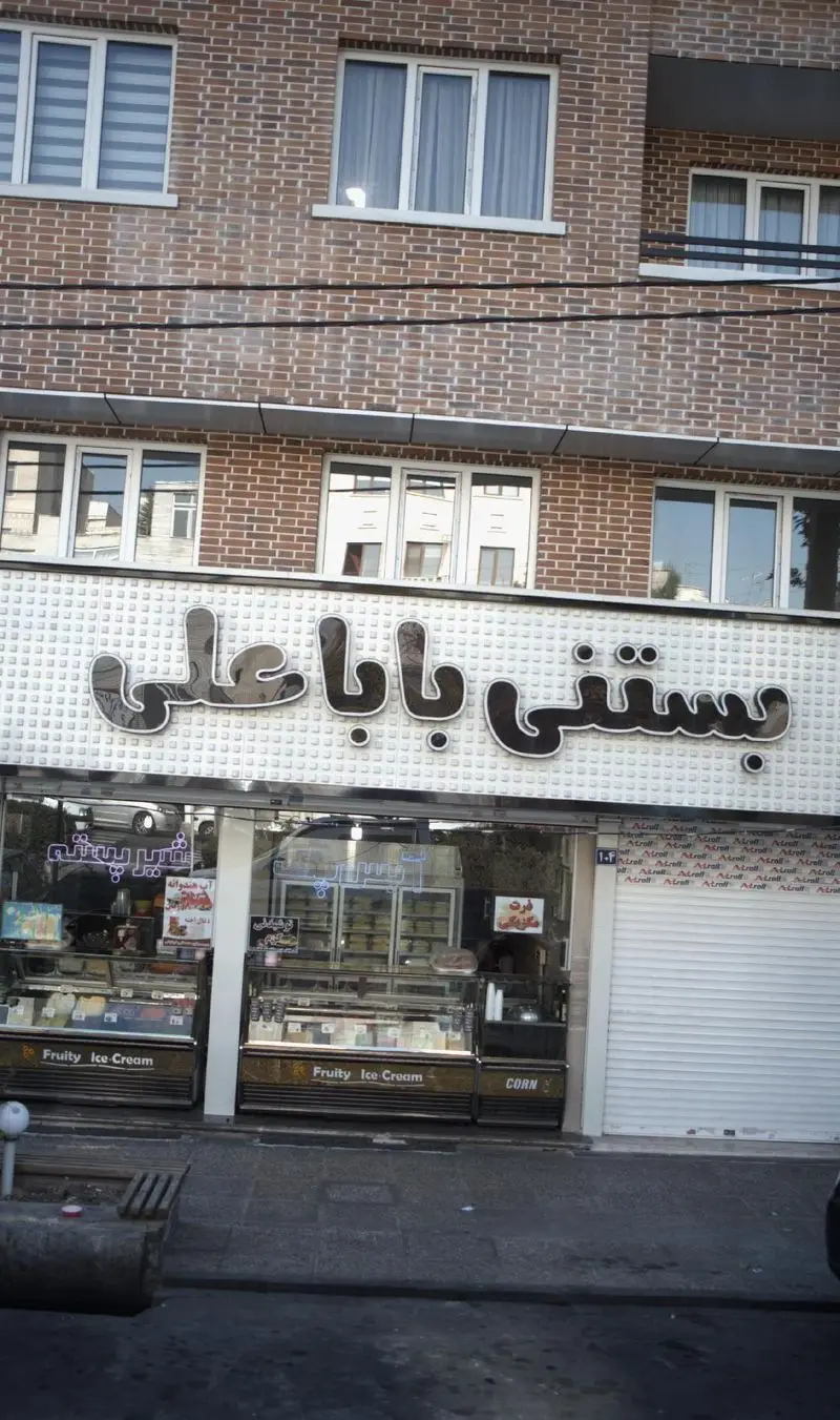 بستنی باباعلی، یک بستنی فروشی پرطرفدار با ویترین‌های جذاب پر از انواع بستنی میوه‌ای و ذرت تازه، آماده پذیرایی.