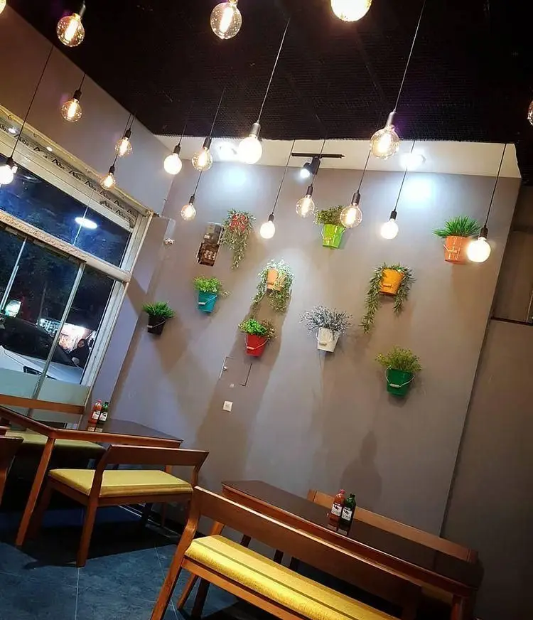 فضای داخلی فست فود شنه با طراحی مدرن، نورپردازی خاص با لامپ‌های ادیسونی و گلدان‌های آویز رنگی، میز و صندلی چوبی و فضای دلنشین.