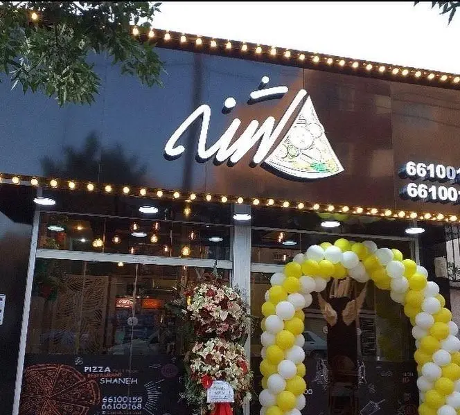 نمای بیرونی و جذاب فست فود و پیتزا شنه با تابلوی روشن، بالون آرایی زرد و سفید، و دکوراسیون مدرن. بهترین پیتزا و فست فود در تهران.
