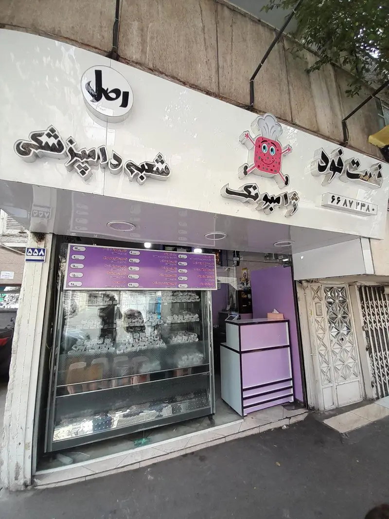 نمای بیرونی فست فود و کیک و شیرینی ژامبونک، شعبه دامپزشکی، با ویترین جذاب از دسرها و شیرینی‌های تازه، همراه با منوی کامل قیمت‌ها.