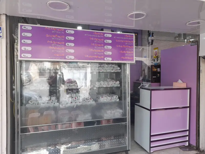 نمای خارجی فست فود ژامبونک، شامل تابلوی منوی غذا و قیمت‌ها، ویترین شفاف پر از ساندویچ‌های آماده و میز پیشخوان.