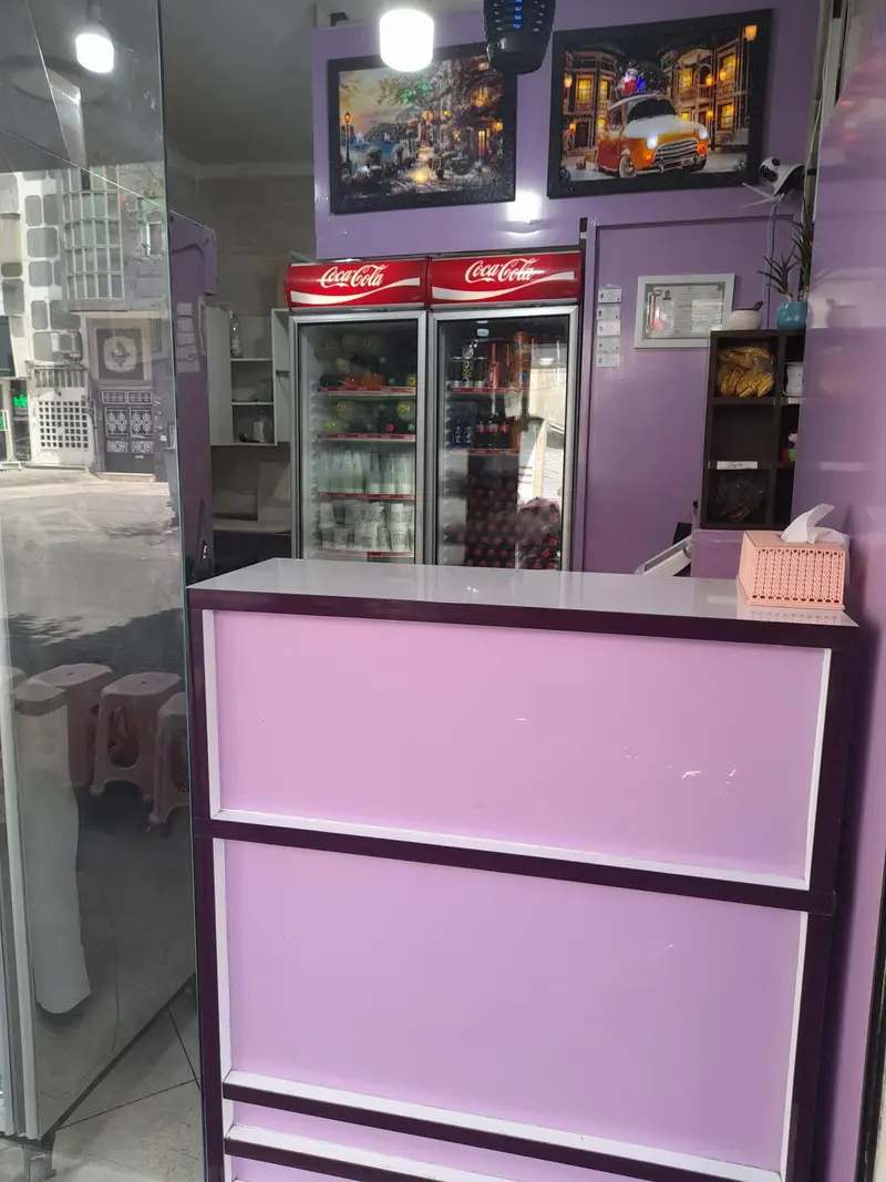 نمای داخلی فست فود ژامبونک شامل پیشخوان مدرن بنفش، دو یخچال نوشیدنی بزرگ کوکاکولا و تزیینات دیواری چشم‌نواز.