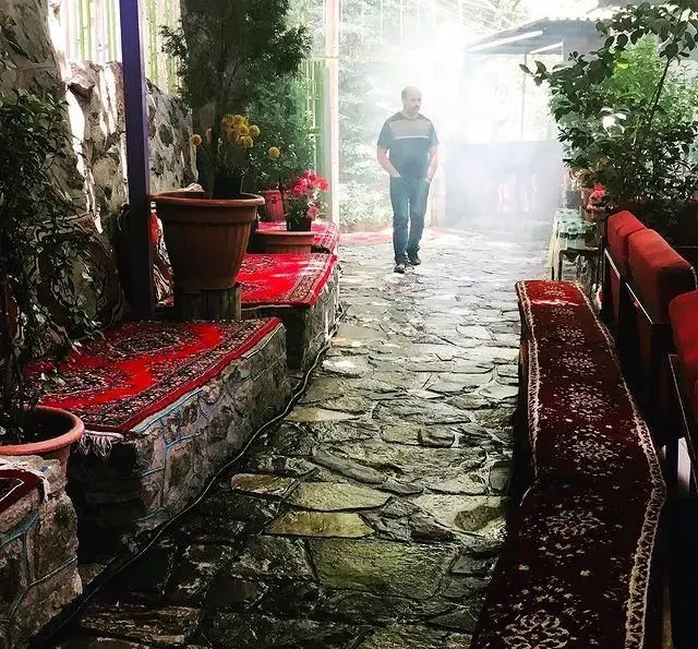 فضای سنتی و دلنشین رستوران جویبار با مسیر سنگفرش، نیمکت‌های فرش شده قرمز و گل‌های زیبا. محیطی عالی برای دیزی و کباب.