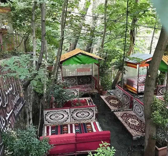 نمایی زیبا از فضای باز و سنتی رستوران جویبار با آلاچیق‌های دلنشین، تخت‌های ایرانی و محیط سرسبز، مکانی عالی برای آرامش و غذا.