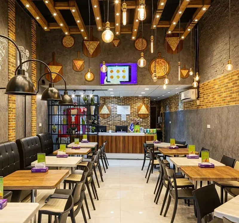 فضای دلنشین و دکوراسیون مدرن فست فود سیب ۳۶۰ با دیوارهای آجری، سقف چوبی، نورپردازی خاص و میز و صندلی‌های راحت برای مشتریان.