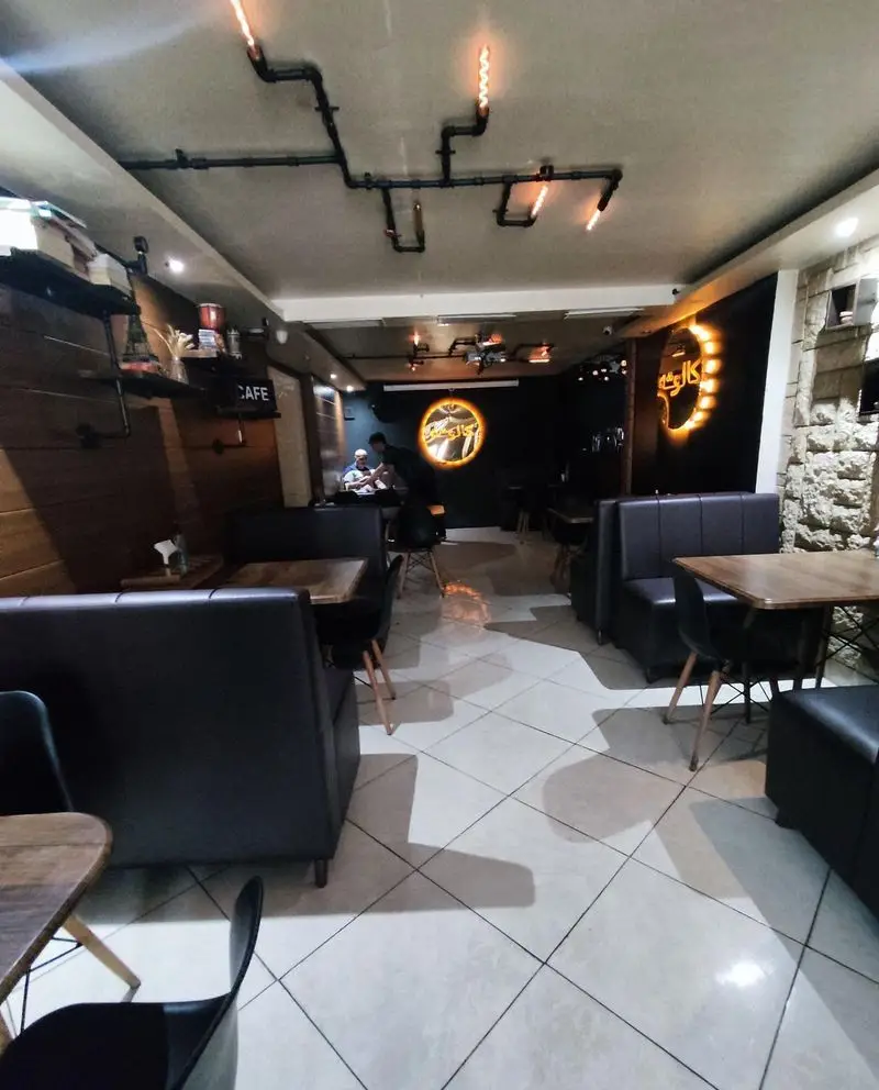 فضای داخلی کافه سئول با دکوراسیون مدرن و صنعتی، مبلمان تیره شیک، نورپردازی خاص و کفپوش سفید. مکانی دنج و جذاب برای مشتریان.