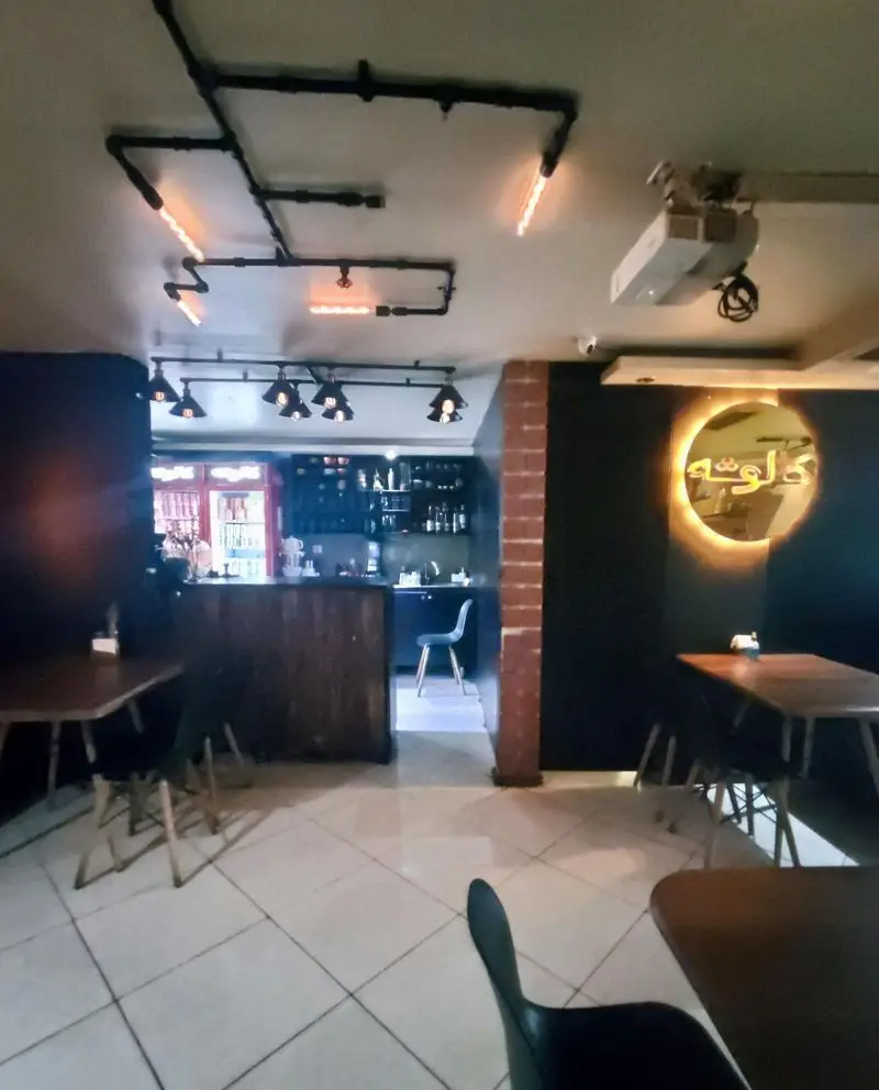 نمایی از فضای داخلی کافه سئول با دکوراسیون مدرن و صنعتی، شامل نورپردازی خلاقانه لوله‌ای و میز و صندلی چوبی، محیطی دنج و جذاب.