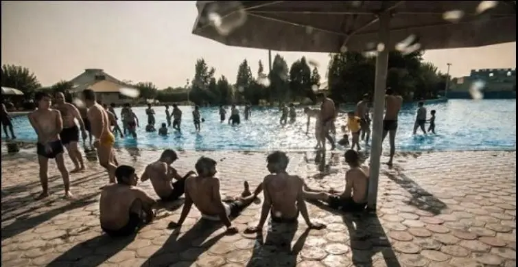 تفریح در پارک آبی آزادگان تهران: مردان و نوجوانان در روزی آفتابی مشغول شنا و بازی در استخر هستند. گروهی نیز در کنار آب استراحت می کنند.