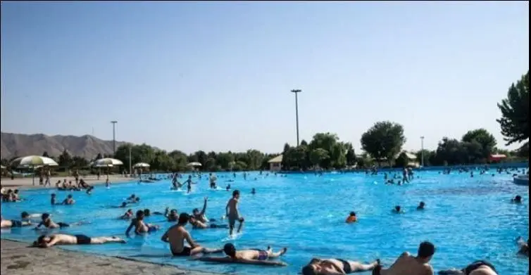 پارک آبی آزادگان: استخری روباز و وسیع مملو از شناگران و افراد مختلف در حال تفریح و آفتاب‌گرفتن در روزی گرم و آفتابی تابستان.