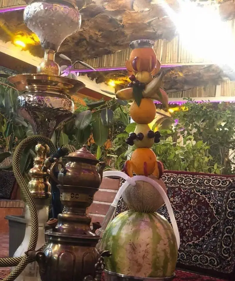 تصویری زیبا از باغ رستوران ایرانی حجت با قلیان میوه‌ای خاص و سنتی، سماور مسی و فضای سرسبز دلنشین و آرام.