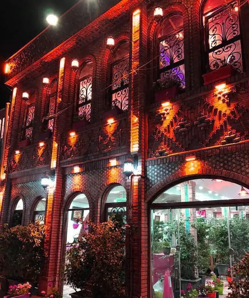 نمای شب رستوران ایرانی باغ رستوران حجت با نورپردازی گرم، معماری سنتی آجری و پنجره‌های فرفورژه. فضایی دلنشین و زیبا.
