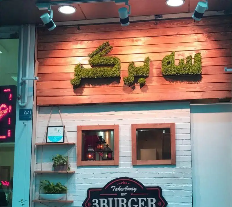 نمای بیرونی کسب و کار فست فود سه برگر با دکوراسیون جذاب شامل تابلوی برجسته سبز رنگ، تابلوی Take Away و آجر سفید.